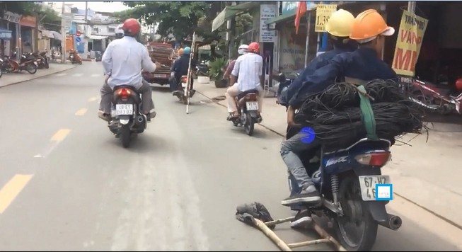 Tay lái xe, chân móc thang tre dài ngoằng trên phố