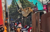 Gầu máy xúc đầy đất công trình chống ngập lơ lửng trên đầu người đi đường 