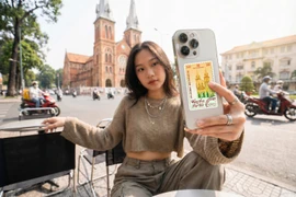 Một bạn trẻ (Gen Z) ăn mặc năng động, tay cầm chiếc điện thoại có ốp lưng trong suốt. Phía sau ốp lưng lấp ló chiếc Thẻ vàng Travel Card 0.1 chỉ rực rỡ màu sắc.