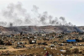 Khói bốc lên đằng sau những chiếc xe bị phá hủy và các tòa nhà bị hư hỏng ở làng Baghouz, tỉnh Deir Ez Zor của Syria gần biên giới với Iraq. 