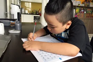 Học sinh lớp 1 đang tập viết chữ ở nhà.