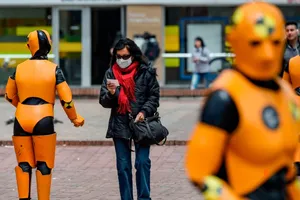 Một phụ nữ đeo khẩu trang đi bên cạnh hai robot giữ trật tự giao thông ở thủ đô Bogota, Columbia ngày 6-3. Ảnh: AFP