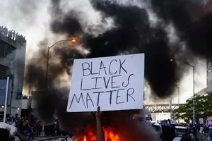 Một người biểu tình giơ biểu ngữ trước một xe cảnh sát bị đốt cháy ở bang Georgia ngày 30-5 (giờ địa phương). Ảnh: AFP