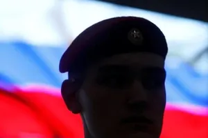 Một binh sĩ Nga đứng trước màn hình hiển thị quốc kỳ Nga.