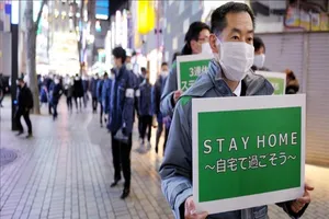 Quan chức TP Tokyo (Nhật Bản) cầm biểu ngữ yêu cầu người dân ở nhà để hạn chế sự lây lan của dịch bệnh. Ảnh: AA