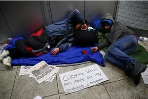 Người vô gia cư trên đường phố London (Anh) và tấm biển “Virus corona làm tất cả tiền tôi xin được biến mất rồi”, ngày 25-3. Ảnh: REUTERS