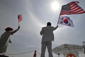 Một người đàn ông và một người phụ nữ vẫy quốc kỳ Mỹ và Hàn Quốc trong buổi lễ kỷ niệm 75 năm thành lập căn cứ thứ tám của quân đội Mỹ, Trại Humphreys, vào ngày 8-6-2019.