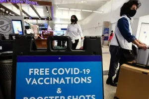 Du khách đi ngang qua một tấm biển ghi dòng chữ cung cấp vaccine COVID-19 miễn phí và các mũi tiêm tăng cường tại một phòng khám ở khu vực dành cho khách quốc tế của Sân bay Quốc tế Los Angeles.