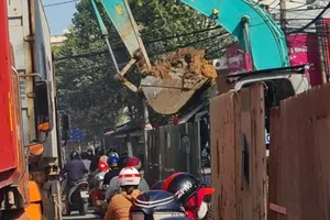 Gầu máy xúc đầy đất công trình chống ngập lơ lửng trên đầu người đi đường 