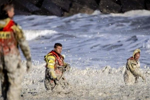 Nhân viên cứu hộ vật lộn với đám bọt biển để tìm kiếm những người lướt sóng mất tích. Ảnh: AFP