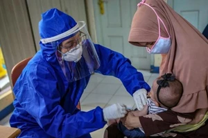 Một nhân viên y tế phải mang đồ bảo hộ để tiêm vaccine cho một em bé ở TP Tangerang, gần Jakarta, Indonesia. Ảnh: REUTERS