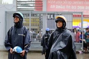 Phụ huynh mặc áo mưa, tay cầm mũ bảo hiểm chờ con trong sân trường. Ảnh: TRƯỜNG GIANG