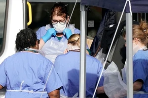 Nhân viên y tế Anh chuẩn bị đưa một người nghi nhiễm khỏi một xe bus công cộng ở TP Wolverhampton, Anh ngày 11-3. Ảnh: AFP