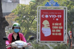Một người dân Hà Nội chạy xe ngang qua một bảng tuyên truyền về phòng, chống dịch COVID-19 (Ảnh chụp ngày 14-4). Ảnh: REUTERS