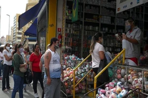 Một nhân viên kiểm tra nhiệt độ khách hàng khi đang xếp hàng để vào cửa hàng mua sắm tại Sao Paulo, Brazil, ngày 10-6-2020.
