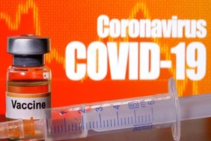 Lọ thuốc dán nhãn vaccine kế bên bảng hiệu ghi chữ COVID-19.