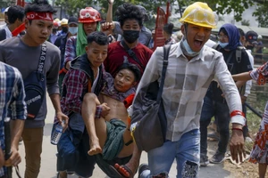 Người biểu tình Myanmar hỗ trợ một người biểu tình khác bị thương do trúng đạn cảnh sát ở TP Yangon ngày 14-3. Ảnh: AP