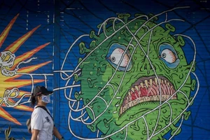 Một người phụ nữ đeo khẩu trang đi ngang qua bức tranh chủ đề COVID-19 khi dịch bệnh tiếp tục bùng phát trên hòn đảo Java, Indonesia, ngày 21-2. 