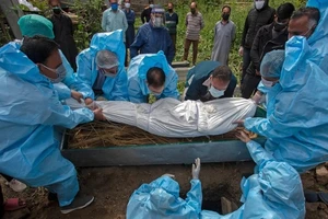 Các nhân viên y tế Ấn Độ mặc đồ bảo hộ đưa thi thể một bệnh nhân COVID-19 vào quan tài. Ảnh: AFP