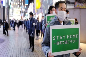 Quan chức TP Tokyo (Nhật Bản) cầm biểu ngữ yêu cầu người dân ở nhà để hạn chế sự lây lan của dịch bệnh. Ảnh: AA