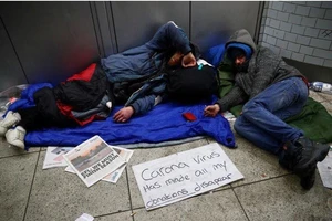 Người vô gia cư trên đường phố London (Anh) và tấm biển “Virus corona làm tất cả tiền tôi xin được biến mất rồi”, ngày 25-3. Ảnh: REUTERS