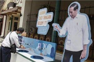 Một người rửa tay bên kệ hình Tổng thống Joko Widodo, ở TP Yogyakarta (Indonesia) ngày 30-3. Ảnh: REUTERS