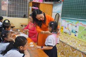 Học sinh lớp 1 trường tiểu học Trần Quốc Thảo, quận 3 được giáo viên ân cần đeo bảng tên. Ảnh: NGUYỄN QUYÊN