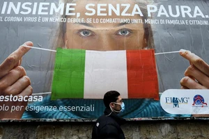 Một người đàn ông đi qua một bảng hiệu về nâng cao ý thức thực hiện các biện pháp ngăn COVID-19 mà chính phủ Ý ban hành ở vùng Naples. Ảnh: GETTY