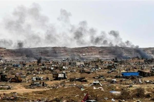 Khói bốc lên đằng sau những chiếc xe bị phá hủy và các tòa nhà bị hư hỏng ở làng Baghouz, tỉnh Deir Ez Zor của Syria gần biên giới với Iraq. 