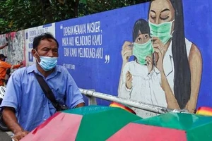 Một người đàn ông đeo khẩu trang đi qua một bức tranh kêu gọi người dân đeo khẩu trang trong bối cảnh dịch bệnh COVID-19 bùng phát trở lại ở Indonesia, ngày 24-7.