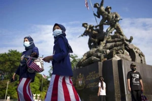 Người dân Malaysia đeo khẩu trang đi bộ trước Tượng đài Quốc gia vào ngày 31-8.