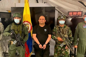 Ông trùm ma túy 50 tuổi bị còng tay và được trình diện trước giới truyền thông, xung quanh là quân đội đứng canh gác với vũ trang đầy đủ.