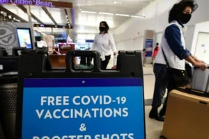 Du khách đi ngang qua một tấm biển ghi dòng chữ cung cấp vaccine COVID-19 miễn phí và các mũi tiêm tăng cường tại một phòng khám ở khu vực dành cho khách quốc tế của Sân bay Quốc tế Los Angeles.