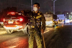 Một sĩ quan cảnh sát đeo khẩu trang và kính chống giọt bắn kiểm tra người lái xe hơi tại một trạm kiểm dịch ở Metro Manila, Philippines.