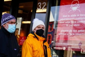 Người dân Mỹ đeo khẩu trang đi ngang qua một biển hiệu của một cửa hàng yêu cầu khách đeo khẩu trang để phòng chống dịch COVID-19, ngày 31-1.