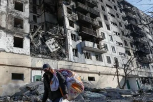 Người dân Ukraine mang đồ di tản khỏi tòa nhà bị các cuộc không kích của Nga phá hủy ở TP Mariupol, vào ngày 28-3.