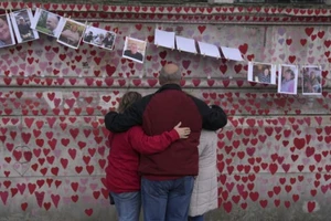 Một gia đình ôm nhau khi đứng trước bức tường tưởng niệm những nạn nhân qua đời vì COVID-19 ở London, Anh quốc, ngày 29-3.