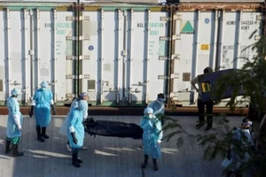 Nhân viên mai táng mặc đồ bảo hộ di chuyển thi thể người chết vì COVID-19 vào thùng chứa lạnh bên ngoài nhà tang lễ vào ngày 10-3.