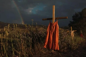 Những chiếc váy đỏ treo trên thánh giá dọc theo một con đường để tưởng nhớ những trẻ em đã chết trong quá khứ tại trường nội trú người da đỏ Kamloops hồi thế kỷ 19 sau khi 215 ngôi mộ không được đánh dấu được phát hiện vào năm 2021.