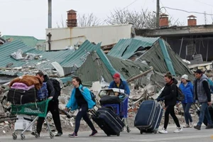Người dân Ukraine mang theo đồ đạc đi qua một tòa nhà bị phá hủy ở Mariupol vào ngày 19-4.