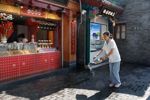 Một người bán hàng ở Bắc Kinh (Trung Quốc) dùng nước để hạ bớt nhiệt nhiệt độ trước cửa tiệm. Ảnh: REUTERS