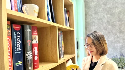 Tác giả bên kệ sách tự tay lắp ghép trong căn nhà trọ của mình. Ảnh: NVCC