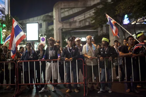 [Caption]Thai anti-government protesters hold national flags as they start massing behind a fence at one of their designated sites in a move to 'shut down' Bangkok on January 12, 2014.