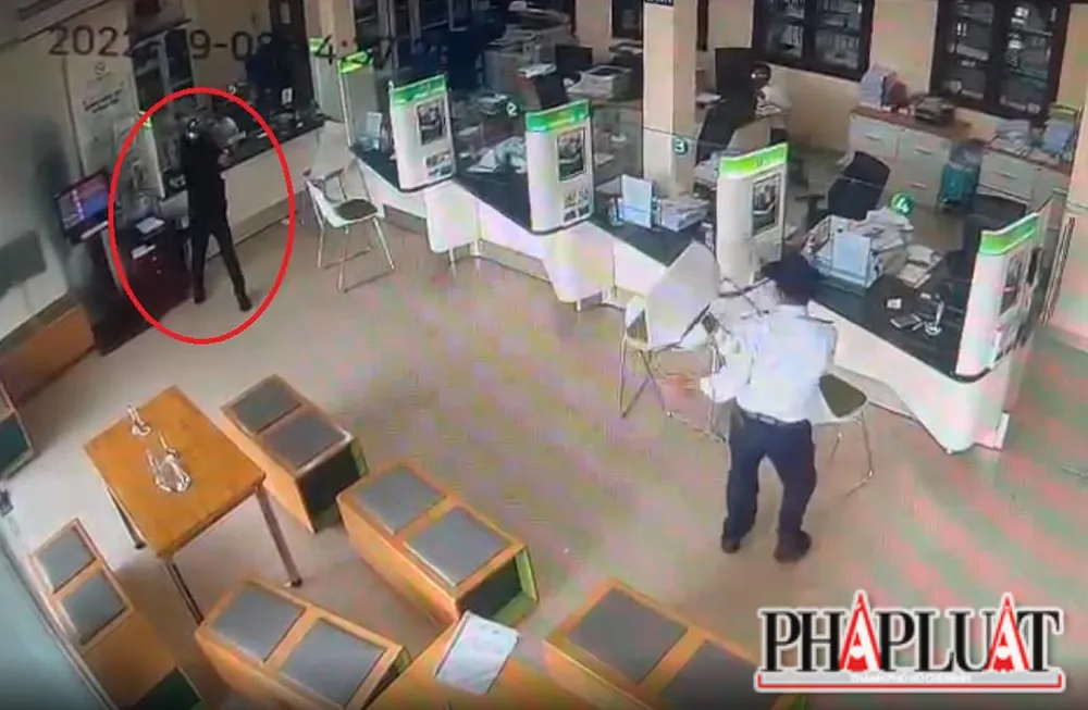 Tên cướp (khoanh tròn đỏ) dùng súng khống chế nhân viên ngân hàng và bảo vệ. Ảnh: VH Tên cướp (khoanh tròn đỏ) dùng súng khống chế nhân viên ngân hàng và bảo vệ. Ảnh: VH
