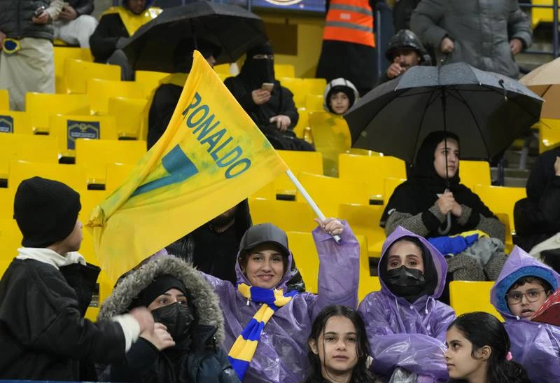 Fan đến xem Ronaldo, tuy nhiên siêu sao của đội chưa thể ra sân được do án phạt treo giò 2 trận ở Anh cũng có hiệu lực tại giải Saudi Arabia. Tuy nhiên Al Nassr cũng thắng 2-0 và có 29 điểm dẫn đầu bảng xếp hạng sau 12 vòng. Ronaldo ngồi trên khu VIP của sân với các lãnh đạo Al Nassr. Một fan nữ tiến đến xin chụp hình chung với Ronaldo. ...OK, chụp nhé. Cho đến nay, áo chính hãng của Ronaldo đã bán được 50 ngàn chiếc. Ronaldo quan sát sân Mrsool qua cửa kính. Ronaldo chào fan khi hiện diện trên khu VIP.