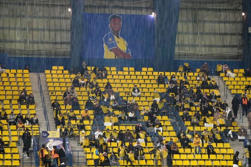 Sân Mrsool có hệ thống thoát nước rất tệ, mưa xuống là sân được ví như... bể bơi. Fan của Al Nassr khoe mới mua được chiếc áo chính hiệu Ronaldo. Ronaldo ngồi xem đồng đội ra sân tiếp Al Taj. Lẽ ra vòng 12 giải Saudi Arabia diễn ra giữa tuần này, song do thời tiết mưa quá kinh khủng, hệ thống điện của sân lại gặp vấn đề nên trận đấu dời lại vào thứ sáu, đó là vòng đấu Al Nassr tiếp Al Taj Fan đến xem Ronaldo, tuy nhiên siêu sao của đội chưa thể ra sân được do án phạt treo giò 2 trận ở Anh cũng có hiệu lực tại giải Saudi Arabia. Tuy nhiên Al Nassr cũng thắng 2-0 và có 29 điểm dẫn đầu bảng xếp hạng sau 12 vòng. Ronaldo ngồi trên khu VIP của sân với các lãnh đạo Al Nassr. Một fan nữ tiến đến xin chụp hình chung với Ronaldo. ...OK, chụp nhé. Cho đến nay, áo chính hãng của Ronaldo đã bán được 50 ngàn chiếc. Ronaldo quan sát sân Mrsool qua cửa kính. Ronaldo chào fan khi hiện diện trên khu VIP.