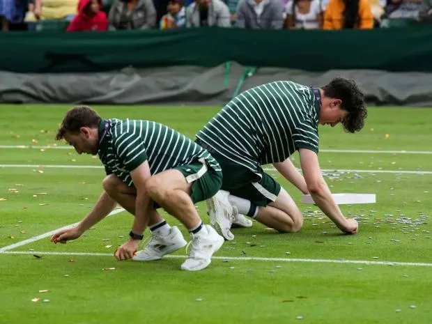 Sang ngày thi đấu thứ năm cũng trên sân 18, những người hoạt động môi trường mặc áo phông với dòng chữ Just Stop Oil tiếp tục rải giấy kim tuyến lên mặt sân, lúc đó đang diễn ra trận đấu Katie Boulter và Daria Saville khiến trận đấu hoãn. Ảnh: S.E Những người vào sân quậy phá bị lực lượng chức năng trong sân bắt giữ và kéo ra khỏi sân. Ảnh: S.E Những mảnh giấy kim tuyến cực mỏng dính vào cỏ rất tốn công &quot;gỡ từng sợi&quot;. Ảnh: S.E Giá cả leo thang, lạm phát khiến tình hình xã hội căng thẳng, nay lại bỏ dầu dùng than và khí gas sẽ gây ô nhiễm môi trường, những người phản đối lập luận như thế. Ảnh: S.E