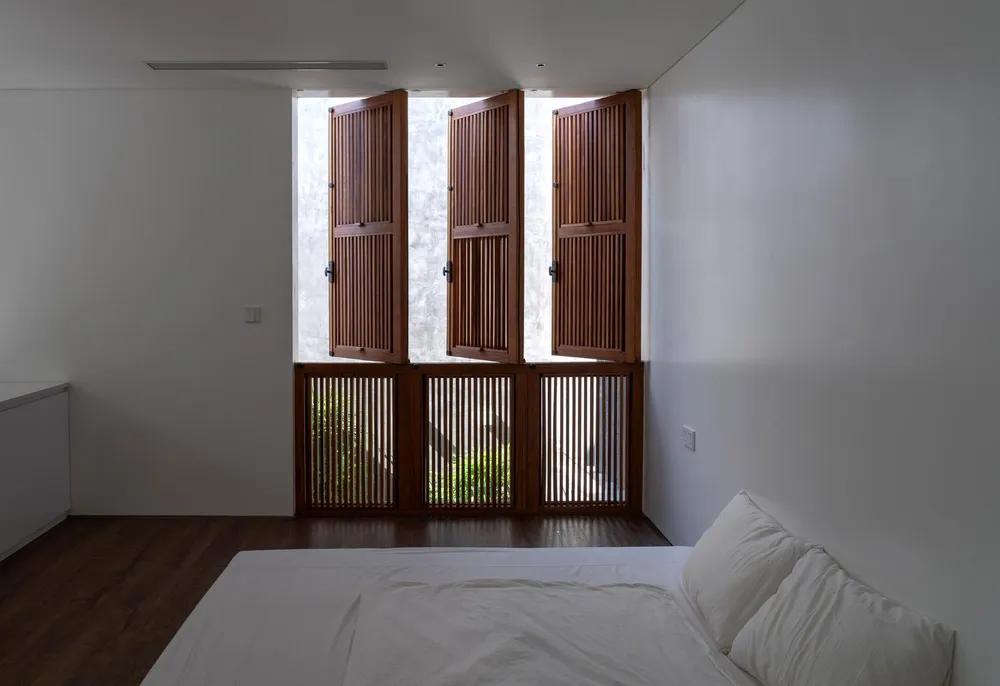 Phòng ngủ kết nối với thiên nhiên bên ngoài khi mở ba cánh cửa gỗ ra.