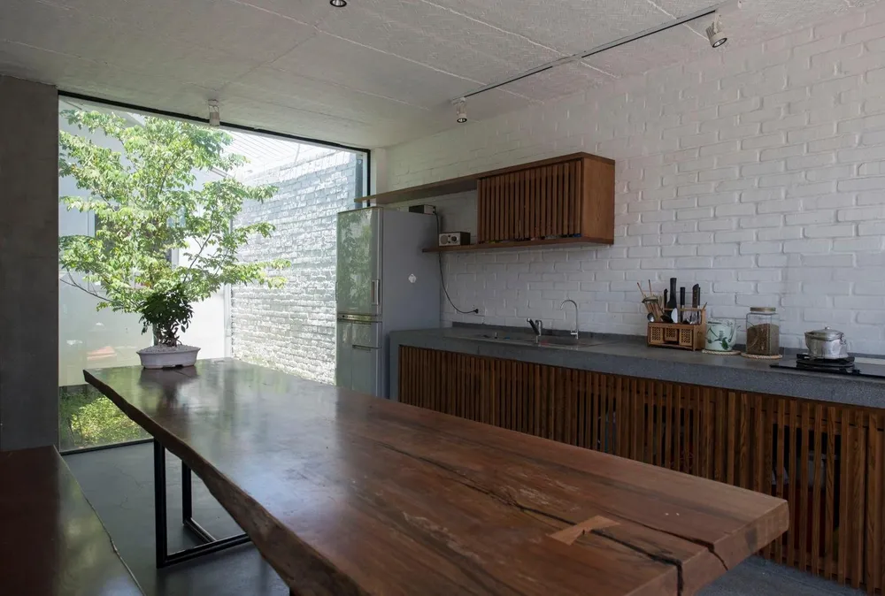 Bếp và bàn ăn bên cạnh khoảng thông tầng có trồng cây xanh khiến không gian này nhận được lượng ánh sáng vừa phải.