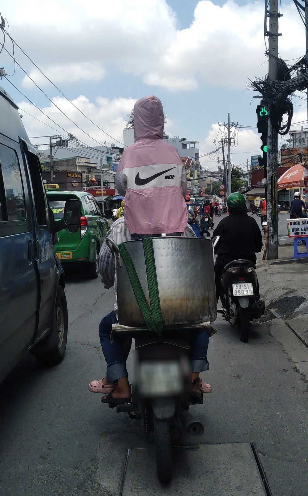 Người đàn ông đi xe máy chở trẻ em đứng trong một chiếc nồi to đặt trên yên xe ở đường Nơ Trang Long, quận Bình Thạnh. Ảnh: THIÊN THẢO